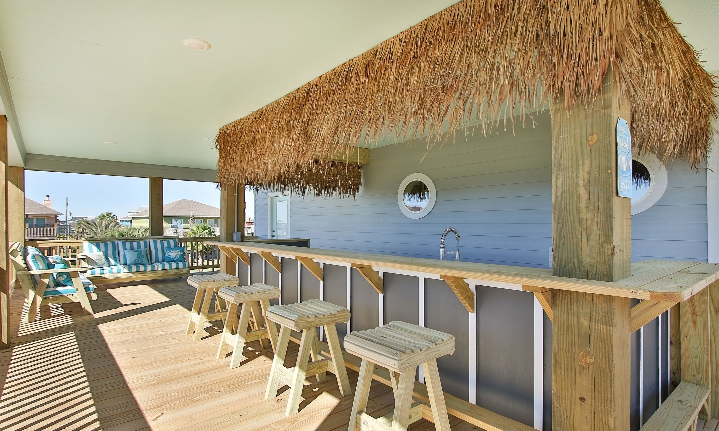 Una terraza de madera con una barra cubierta de paja, taburetes de madera y vistas al océano.