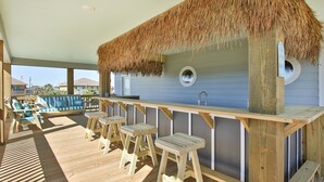 A wooden deck with a thatched roof bar area, wooden stools, and a view of the ocean. - S.S. Esmeralda-Newly built home-3min from beach (Bolivar Peninsula)