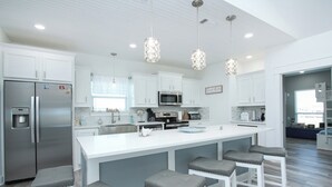 A modern kitchen with white cabinetry, stainless steel appliances, and a central island with bar stools. - S.S. Esmeralda-Newly built home-3min from beach (Bolivar Peninsula)