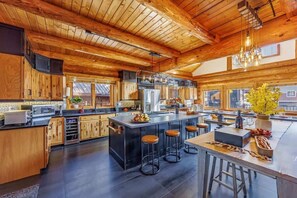 A spacious kitchen with wooden cabinets, a large island with stools, and a view through the windows. - Fire Lodge Premier Family Cabin at Snoqualmie Pass (Snoqualmie Pass)