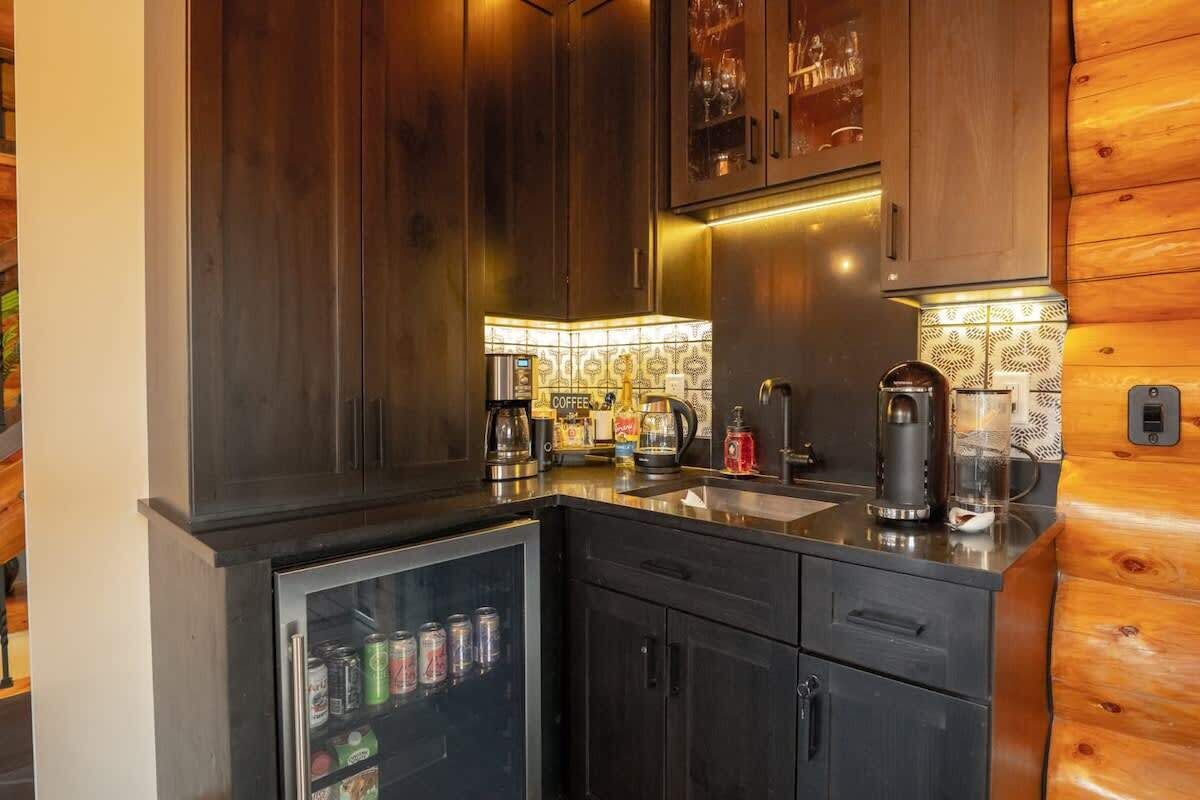 A compact kitchen with dark wooden cabinets, a built-in coffee maker, and a small refrigerator stocked with beverages.