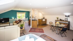 A spacious loft with a high ceiling, a cozy living area with a sofa and TV, a dining area with a glass table, and a kitchen with wooden cabinets.