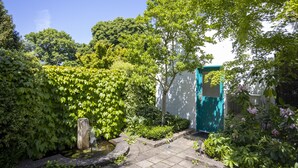 A garden with a stone pathway, lush greenery, and a building with a blue door.