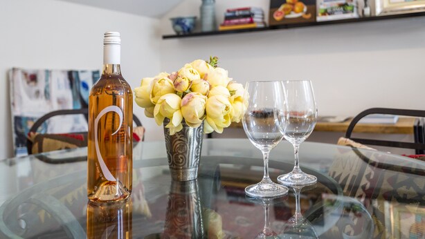 A table with a bottle, a vase with flowers, and two glasses.