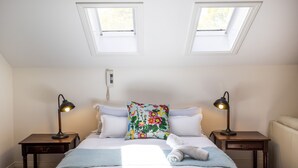 A bedroom with a bed, two bedside tables, a floral pillow, a blue blanket, and two skylights.