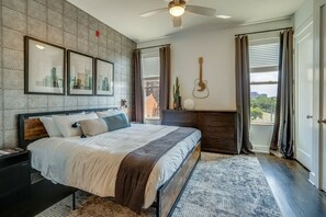 A bedroom with a bed, a nightstand, a dresser, a guitar, and a cityscape view.