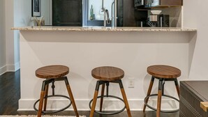 A modern kitchen with a central island, pendant lights, and wooden stools. - Lofts at 30th-Urban Sky Suite-Walk to restaurants! (Nashville)