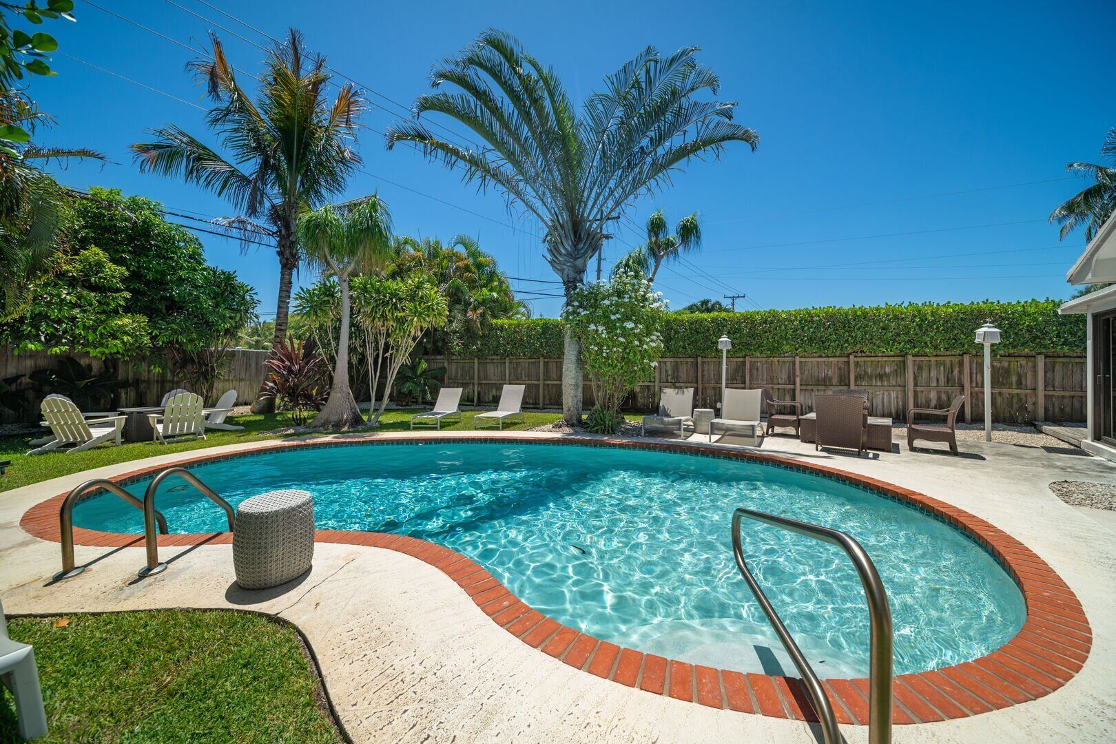 A swimming pool with a brick border, surrounded by lounge chairs and palm trees.