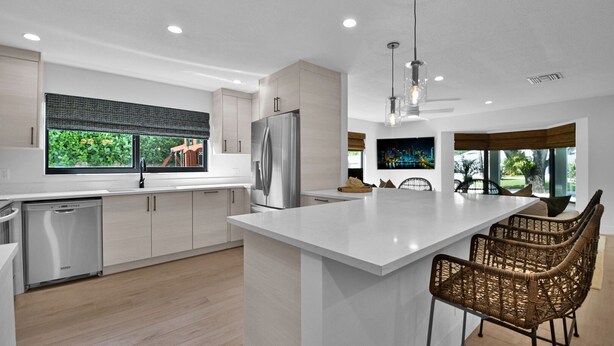 A modern kitchen with a large island, stainless steel appliances, and wicker chairs. - 501 Managed By Brampton Park (Delray Beach)