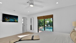 A bedroom with a bed, a ceiling fan, a TV, and a view of an outdoor swimming pool. - 501 Managed By Brampton Park (Delray Beach)