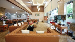 A spacious lobby with leather sofas, a TV screen, and a large window offering a view of the outside.