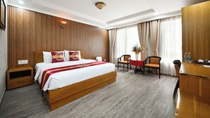 A hotel room with a large bed, wooden panel walls, a wooden desk, and a dining table with chairs.