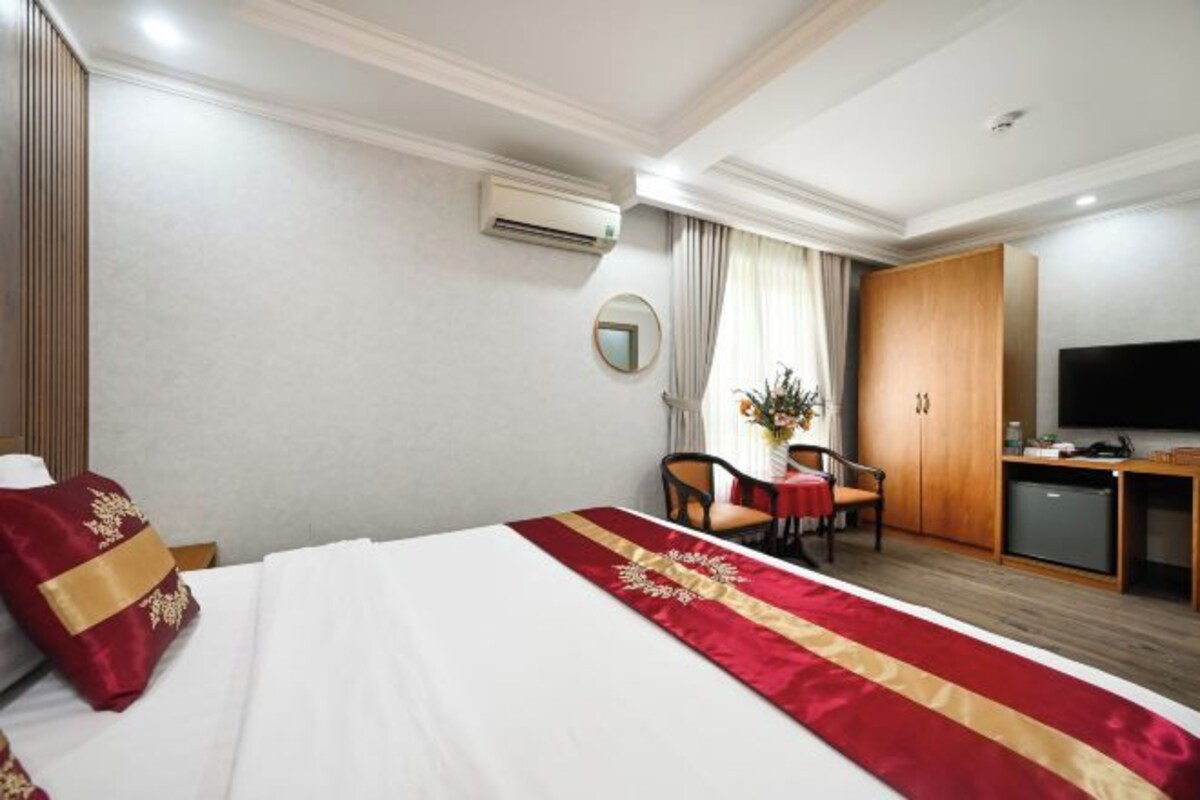 Quarto de hotel com cama, escrivaninha, televisão e guarda-roupa.