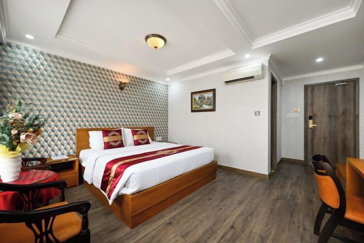 Habitación de hotel con cama, escritorio, silla, una mesita pequeña y una pared con diseño geométrico.