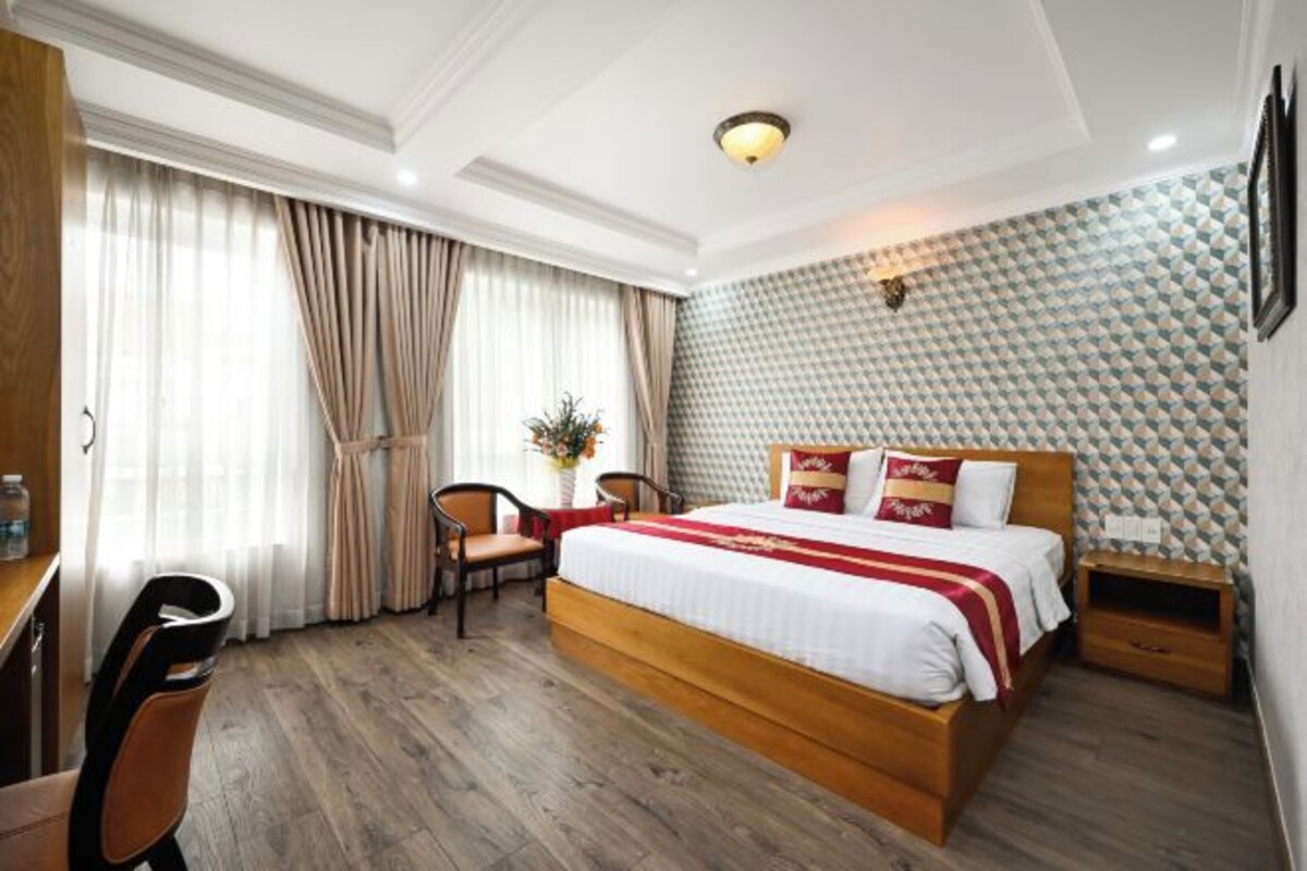 Quarto de hotel com cama de madeira, uma escrivaninha, uma cadeira e janela com cortinas.