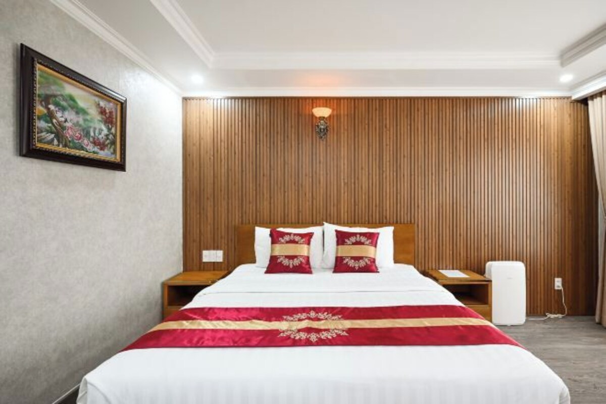 Quarto de hotel com cama, parede de madeira, mesa de cabeceira, luminária e uma pintura na parede.