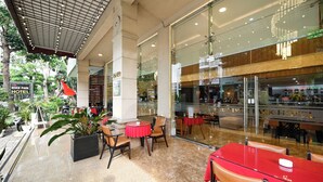 A hotel lobby with glass walls, indoor plants, and red tables and chairs.