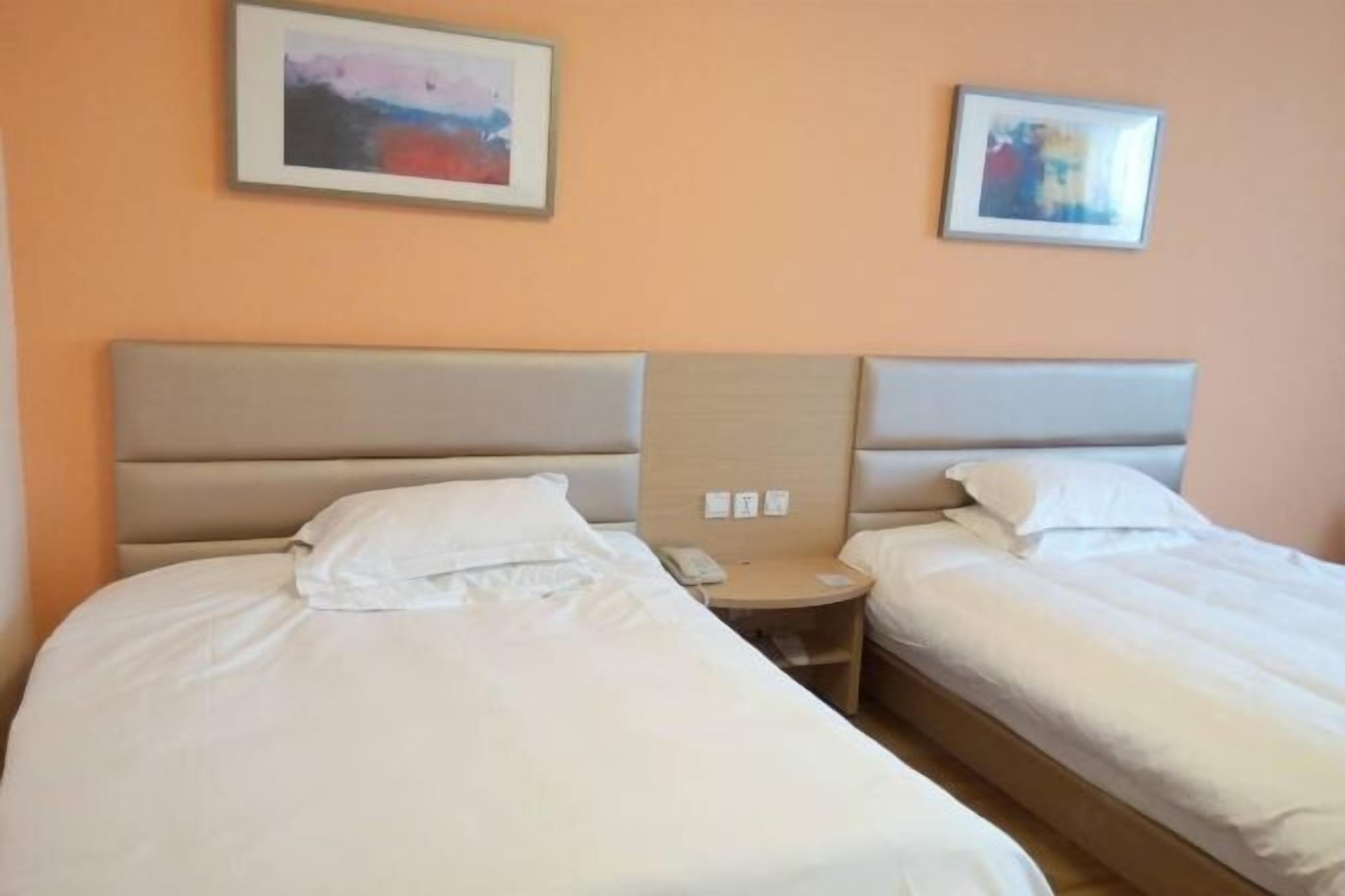 A hotel room with two beds, a bedside table with a phone, and two framed pictures on the wall.