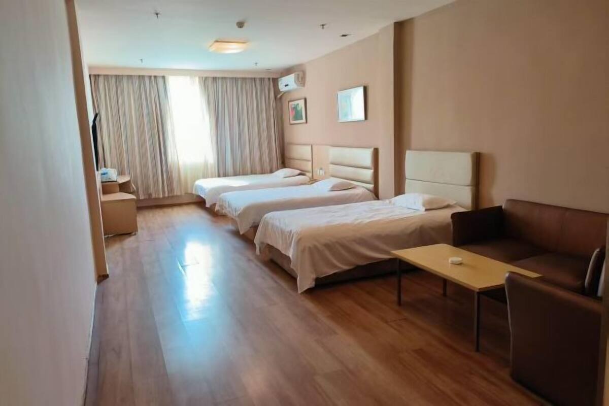 A hotel room with two beds, a sofa, a small table, and a window with curtains.