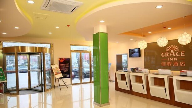 A hotel reception area with a modern design, including a reception desk, a green pillar, and a large window offering a view of the street. - Grace Inn (Yutai Bus Station) (Yutai)