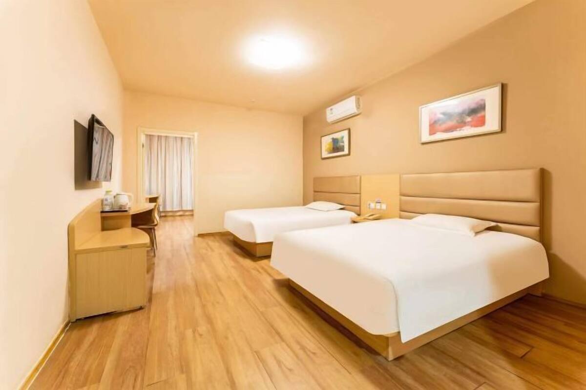 A hotel room with two beds, a desk, a chair, and a TV mounted on the wall.
