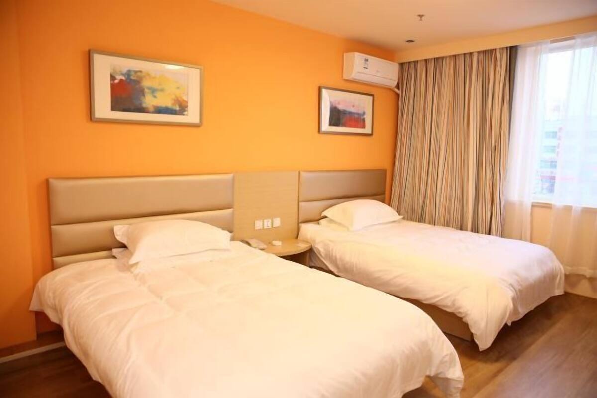 A hotel room with two beds, a large window with curtains, and two framed pictures on the wall.