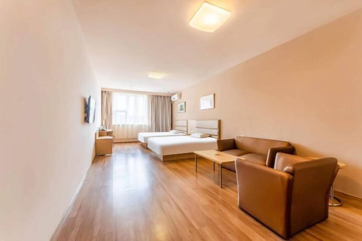 A hotel room with a large bed, a sofa, a small table, and a window with curtains.
