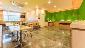 A modern dining area with a long table and chairs, a kitchen area with a green accent wall, and a large window providing natural light. - Grace Inn (Yutai Bus Station) (Yutai)