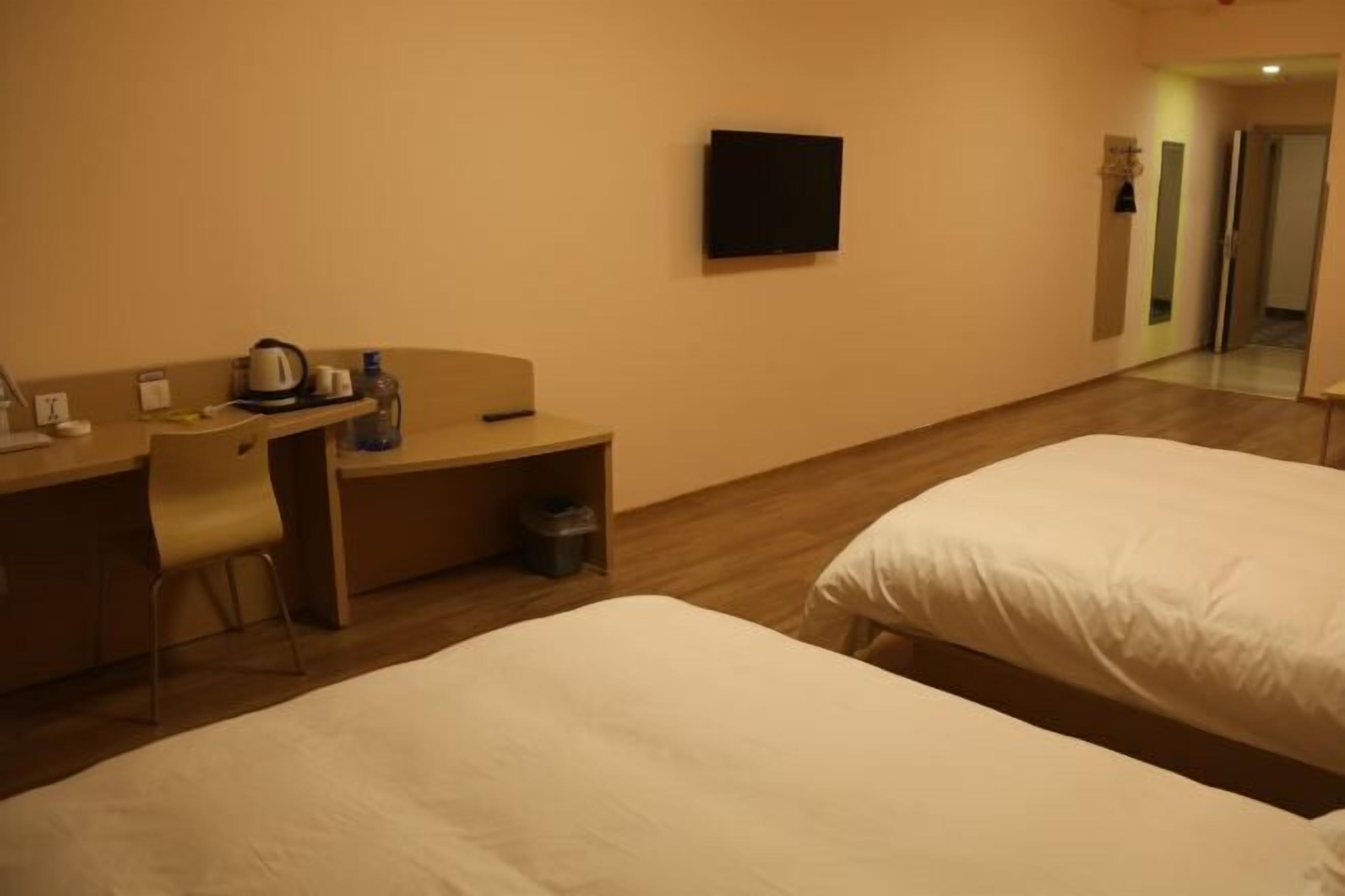 Habitación de hotel con dos camas, un escritorio con silla, televisor y espejo.