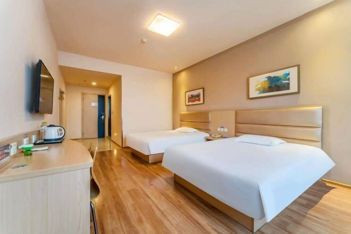 A hotel room with two beds, a desk with a kettle, and a painting on the wall.