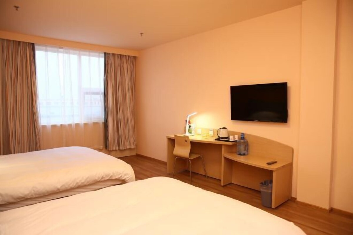 A hotel room with two beds, a desk with a chair, a television, and a window with curtains.