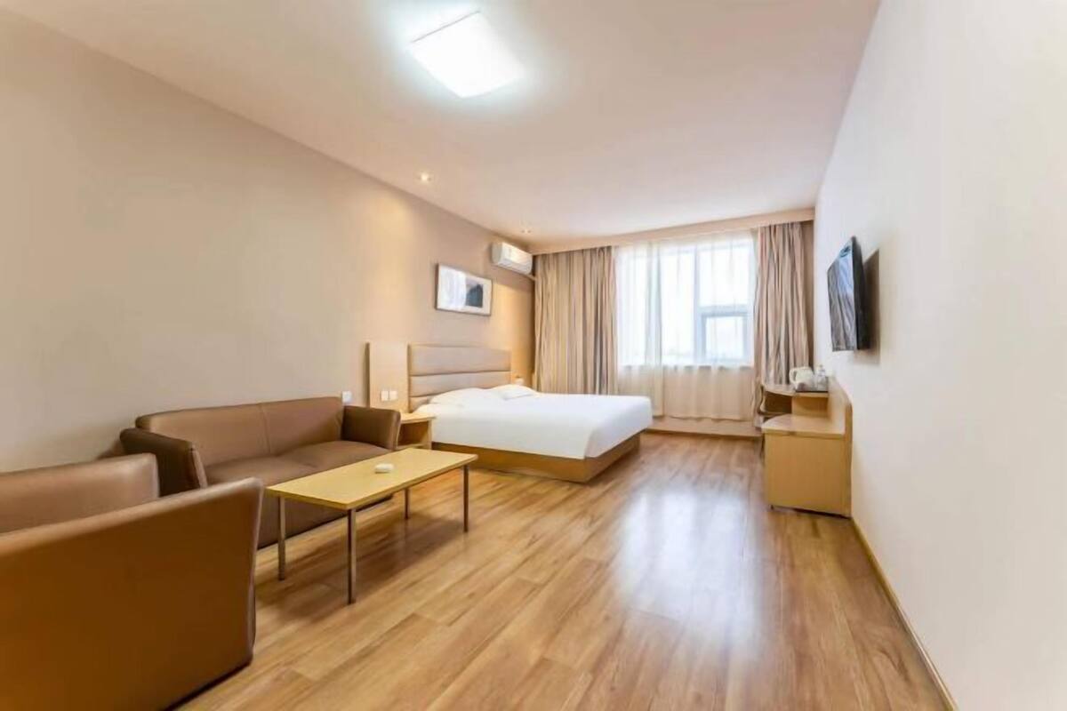 A hotel room with a bed, a sofa, a small table, and a TV.