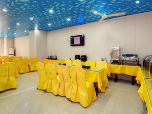 Ein Konferenzraum mit Tischen, Stühlen, einem Deckenventilator, einem Fernseher und einem Büfett.