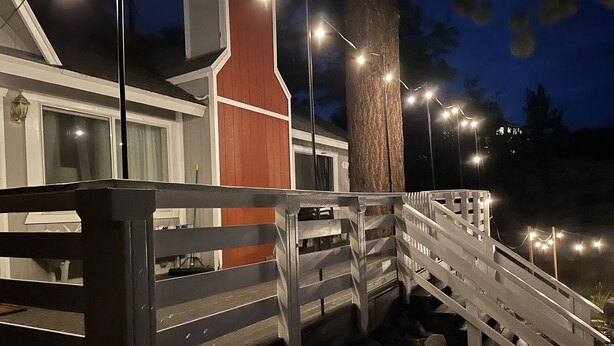 A wooden deck with a white railing, a stone pathway, and a building with a red accent wall and a window. - Romantic Winter Escape with Mountain Views (Running Spring (Arrowbear lake area))