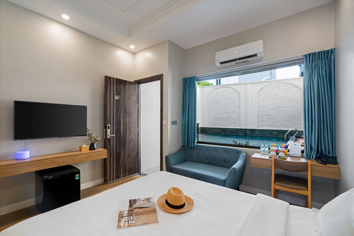 A hotel room with a bed, a TV, a desk with a computer, a window with curtains, and a view of a pool.