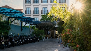 A white multi-story building with balconies, a covered parking area, and potted plants. - Le Cap Hotel & Apartment (Da Nang)