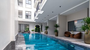 A modern indoor swimming pool with clear blue water, surrounded by a white interior and potted plants. - Le Cap Hotel & Apartment (Da Nang)