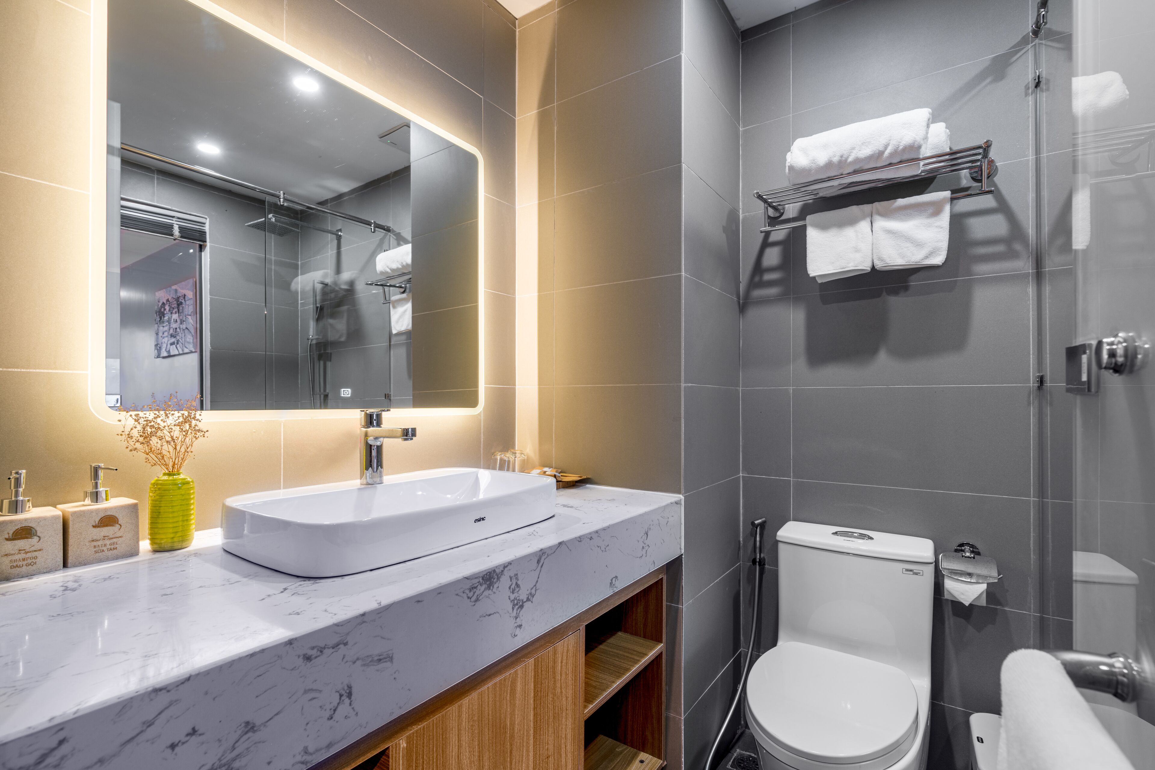 Un baño moderno con un espejo grande, un lavamanos blanco y una ducha con mampara de vidrio.