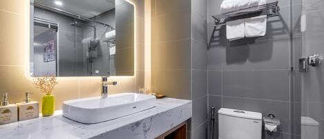 Un baño moderno con un espejo grande, un lavamanos blanco y una ducha con mampara de vidrio.