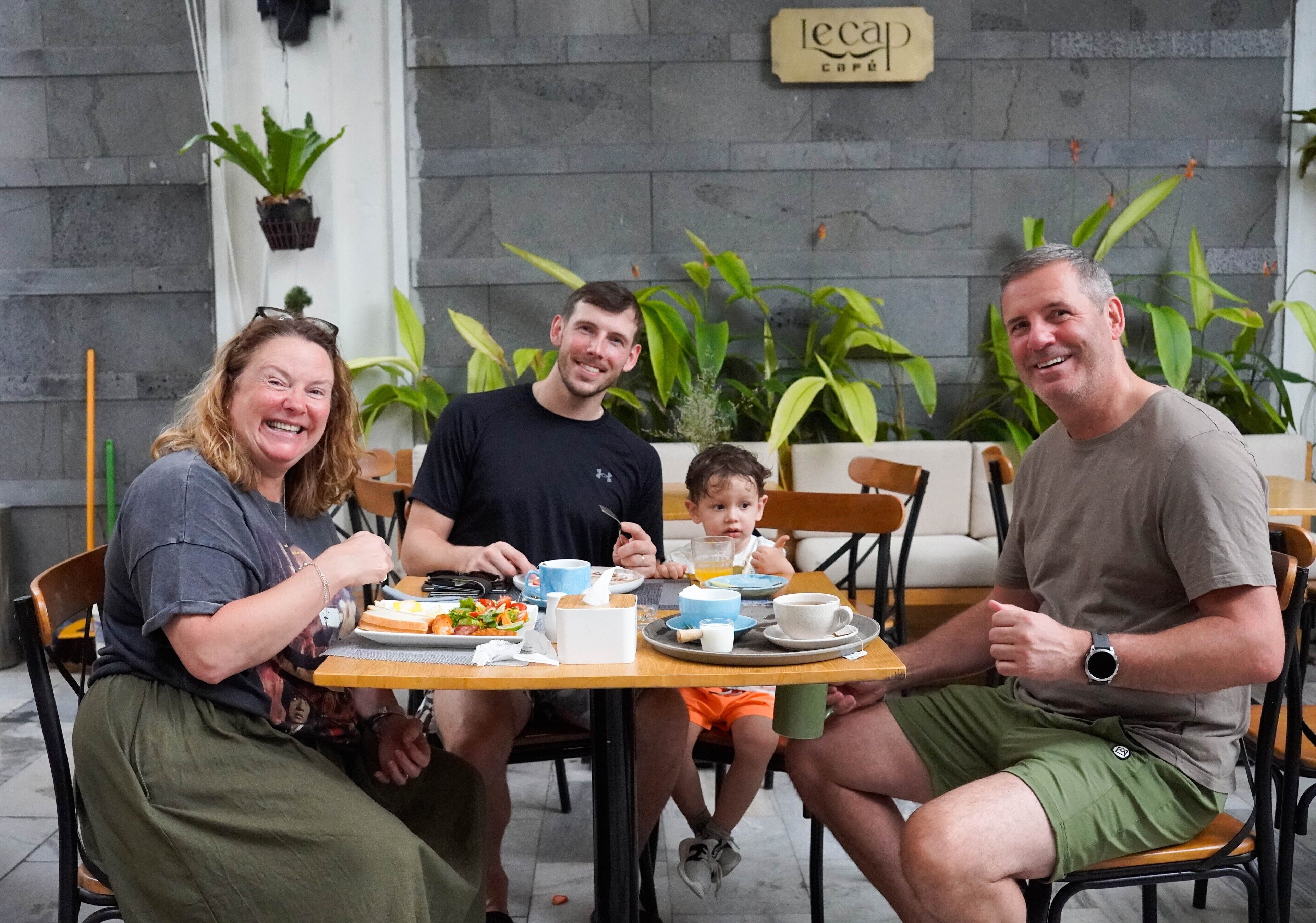 A family dining at a cafe with a stone wall and potted plants in the background.