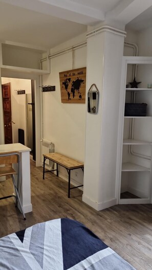 A room with a wooden floor, a bed with a patterned blanket, a bench, a wall-mounted map, and a radiator.
