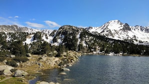 A clear mountain lake with rocky shores and snow-capped peaks in the background.