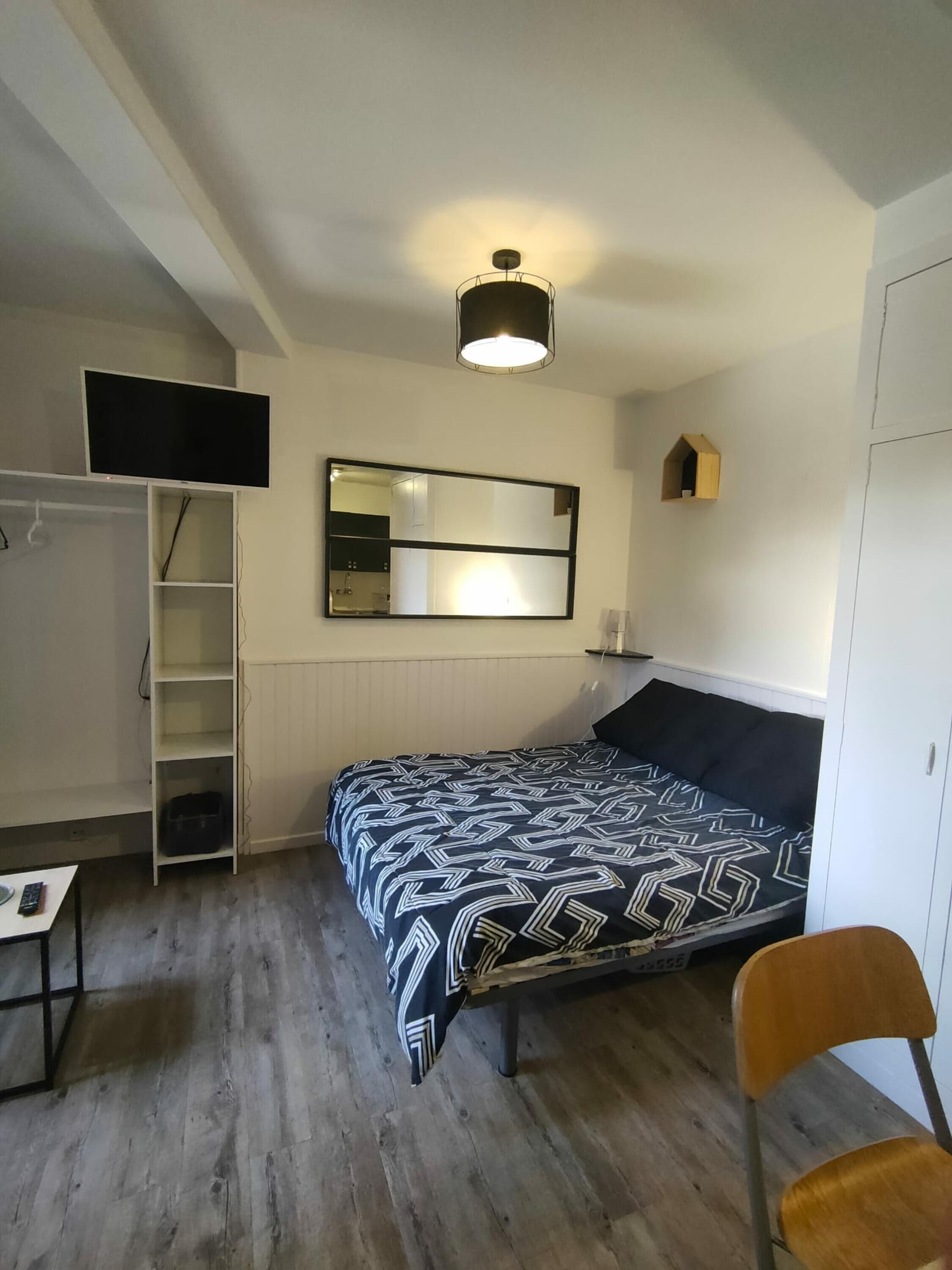 A bedroom with a bed, a desk, a chair, a wardrobe, a TV, a mirror, and a ceiling light.