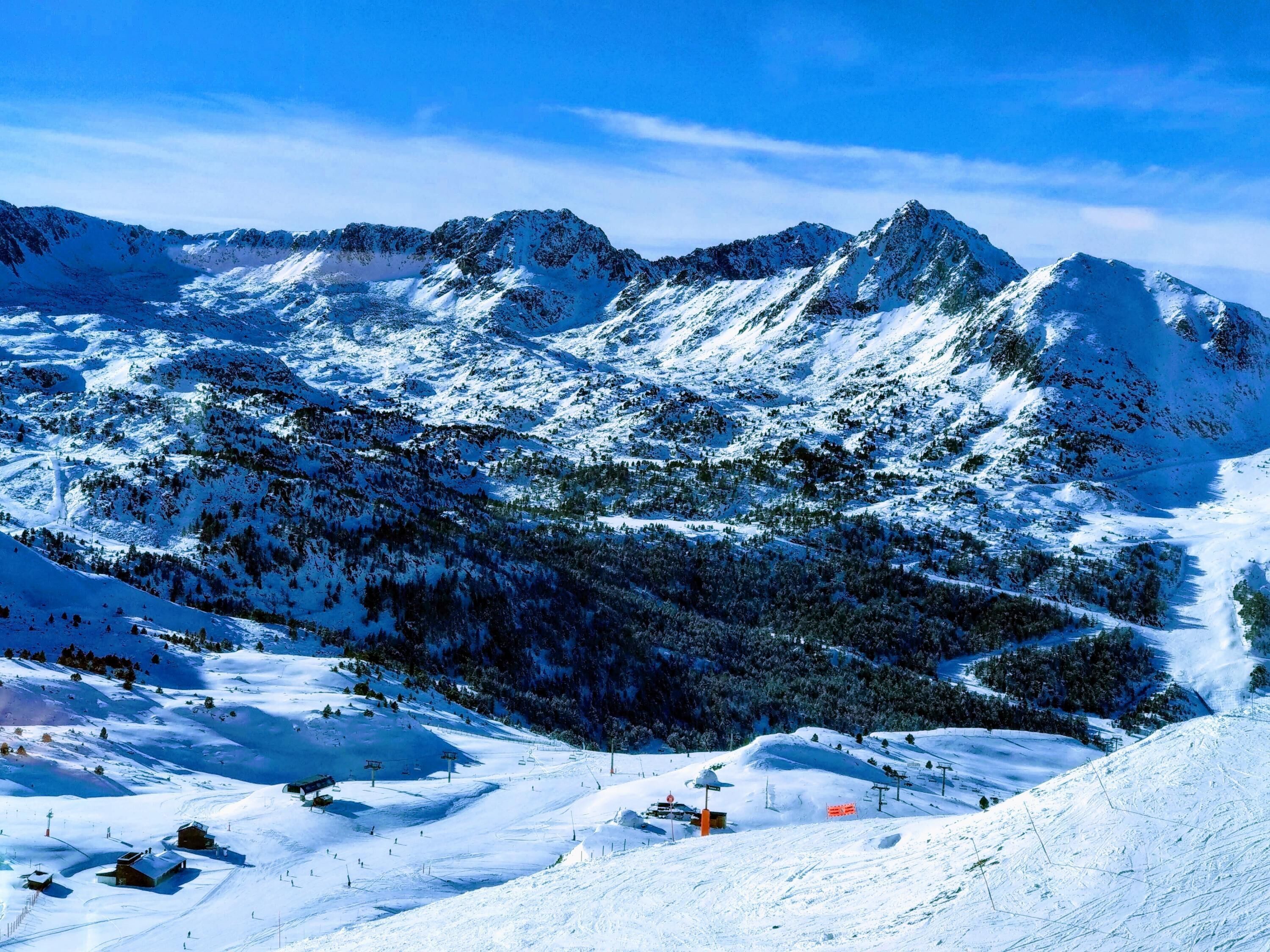 Un paysage de montagne enneigé, avec des pistes de ski, des remontées mécaniques et un petit chalet.
