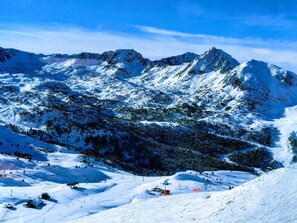 Paisaje nevado de montaña con pistas de esquí, remontes y un pequeño albergue.