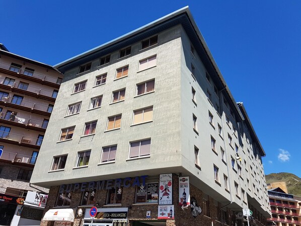 Un edificio de varios pisos con un letrero que dice 'SUPERMERCAT' en la planta baja, indicando un supermercado.