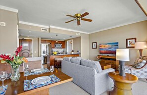 A modern living room with a grey sofa, a wooden coffee table, and a dining area with a set table. - Maui Resort Rentals: Honua Kai - 4 Total Bedrooms,  6th Floor Deluxe Ocean and Lush Mountain Views! (Lahaina)