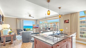 Una cocina moderna con una isla grande, un comedor con vistas y una sala de estar con ventilador de techo y televisor.