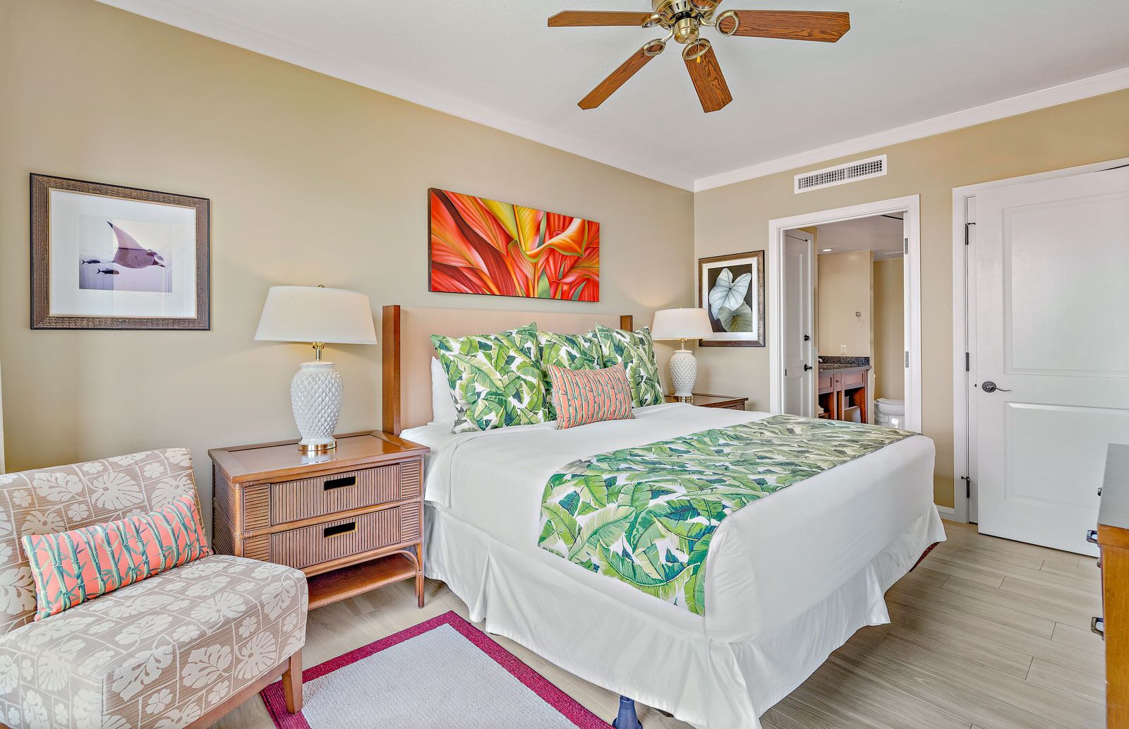 Une chambre d’hôtel comprenant un lit, une table de chevet, une chaise, un ventilateur de plafond et des œuvres d’art accrochées aux murs.