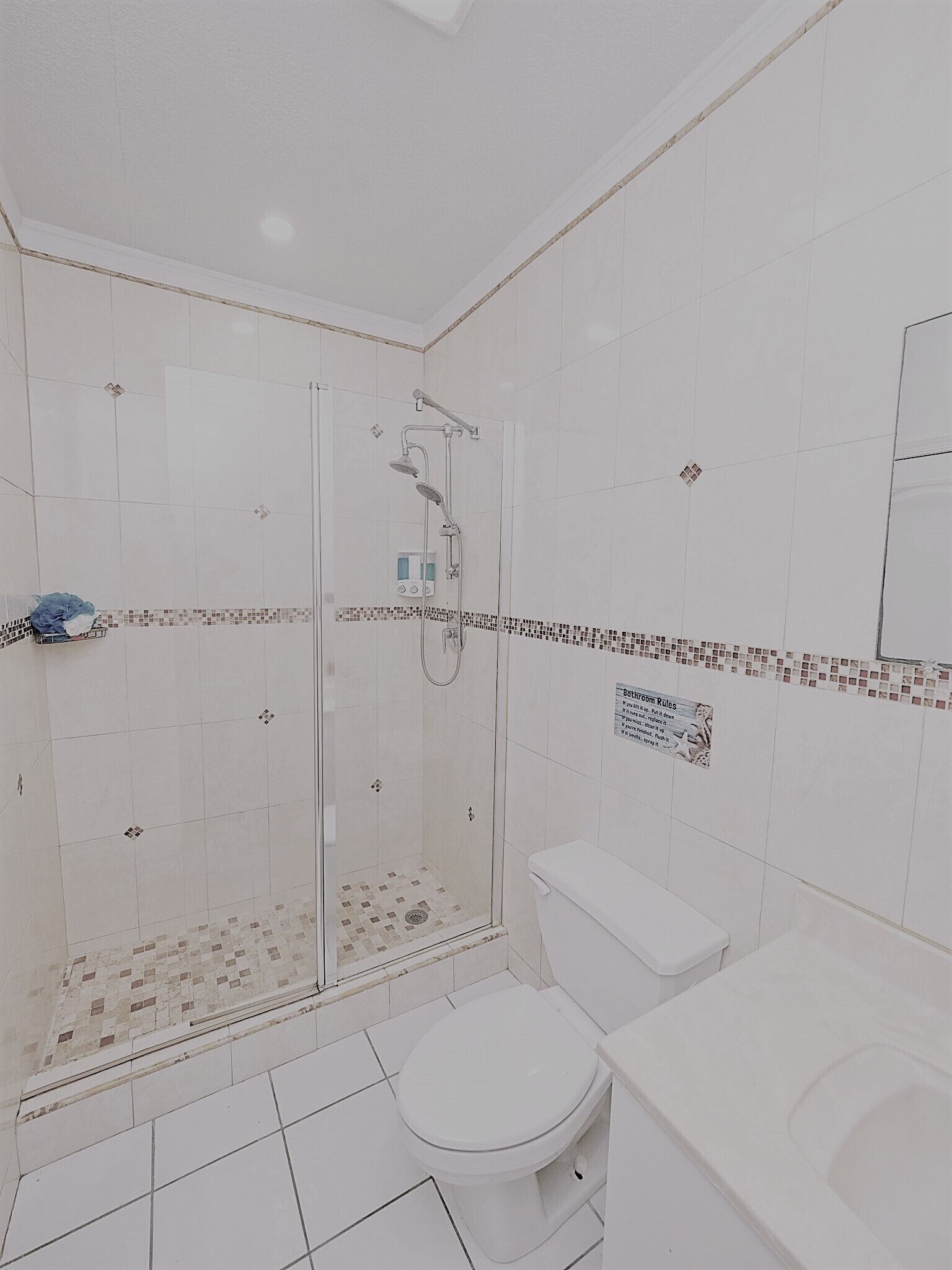 A modern bathroom with a glass-enclosed shower, white tiles, and a toilet.